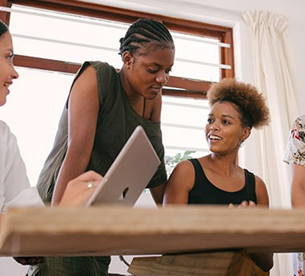 Four Women Are Seated At A Table, Collaborating Over A Laptop